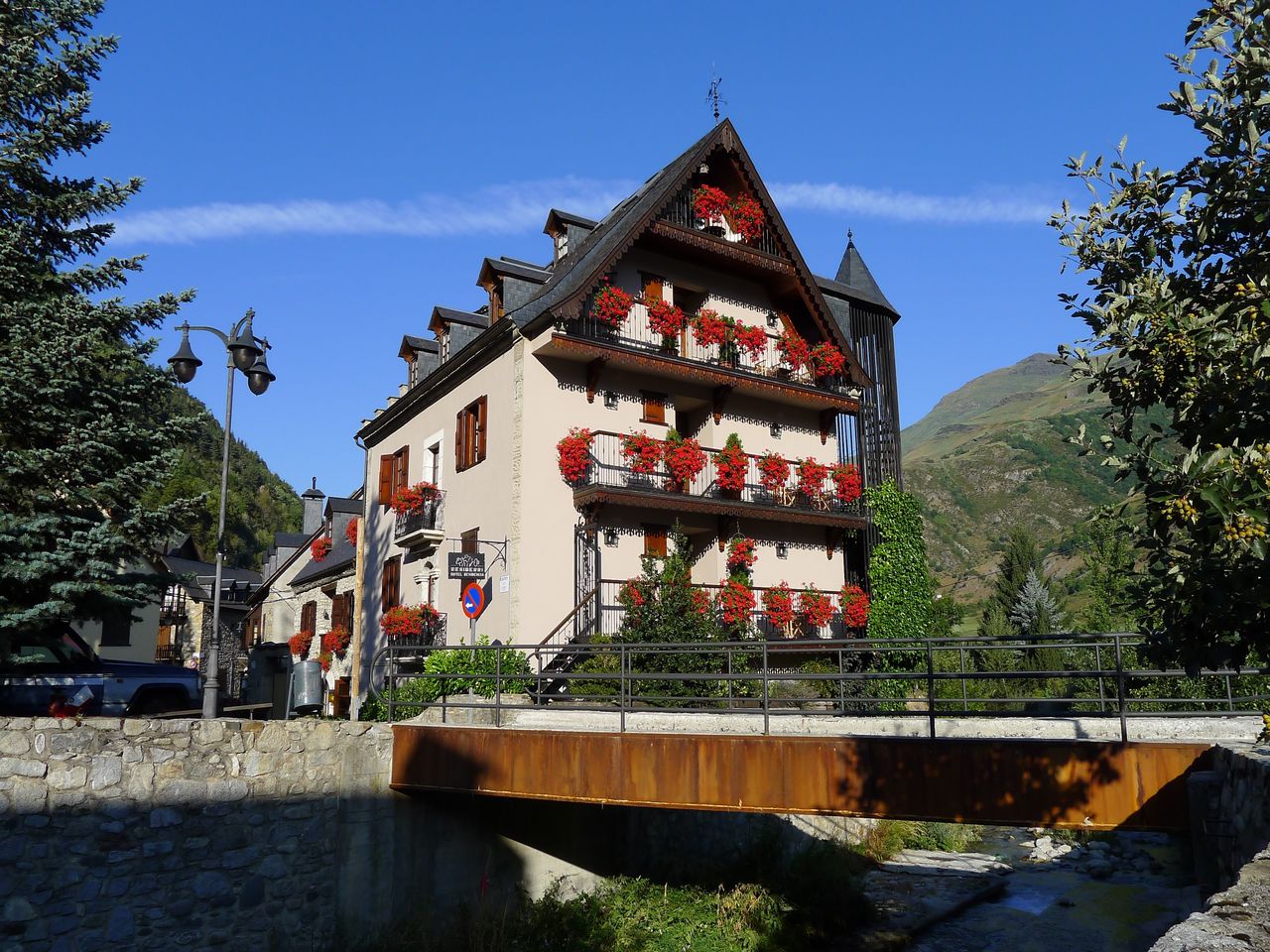 Fachada del hotel con geranios rojos en los balcones. En primer plano el puente sobre el río